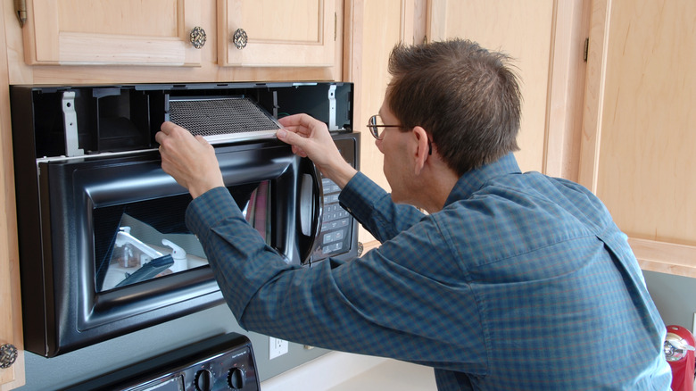 A person replacing their microwave filter.