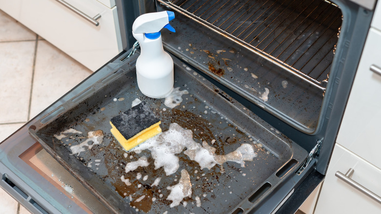 A dirty oven covered in cleaner with a spray bottle and a sponge.