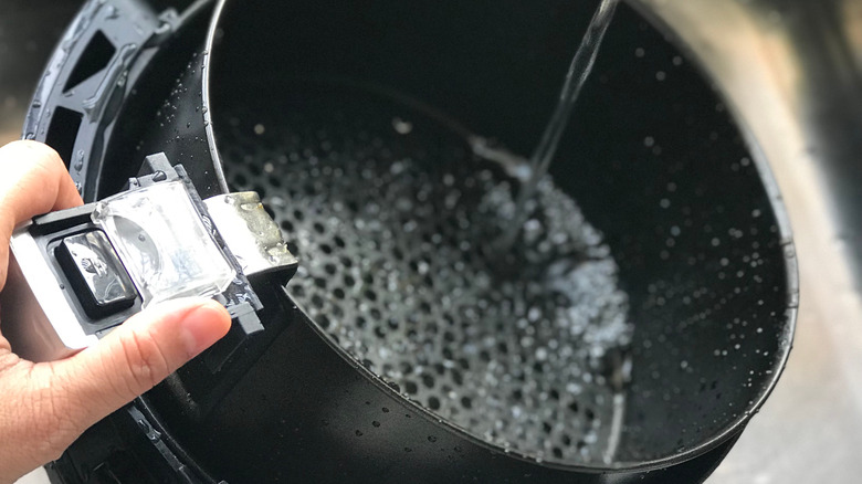 An air fryer basket under running tap water