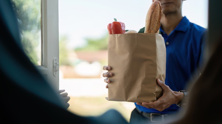 A man holds a filled paper grocery bag at the door of a house