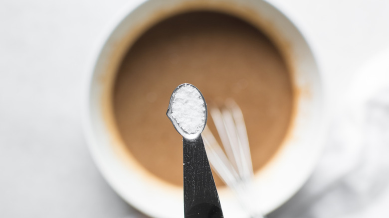A teaspoon filled with baking soda hovers over a bowl of batter