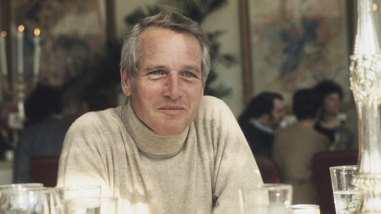 Paul Newman smiles while sitting at a table.
