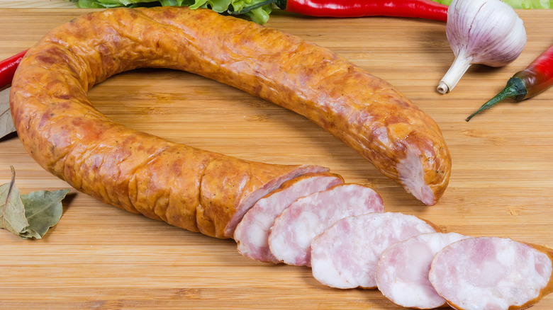 Sliced ring bologna on a cutting board surrounded by garlic and peppers