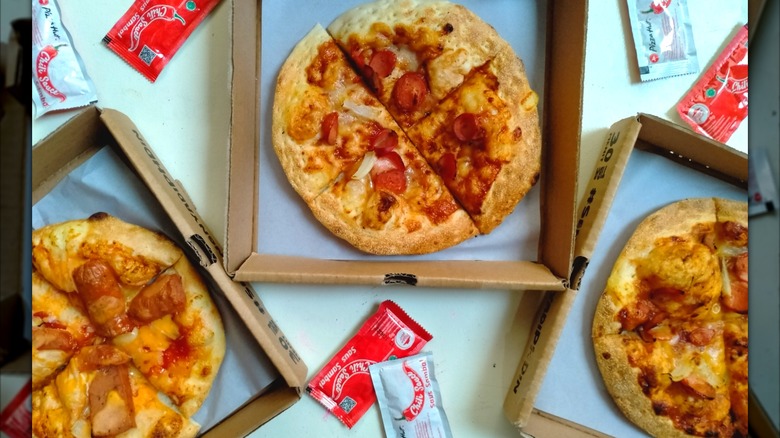 Various Pizza Hut pizzas in take-out boxes with sauces