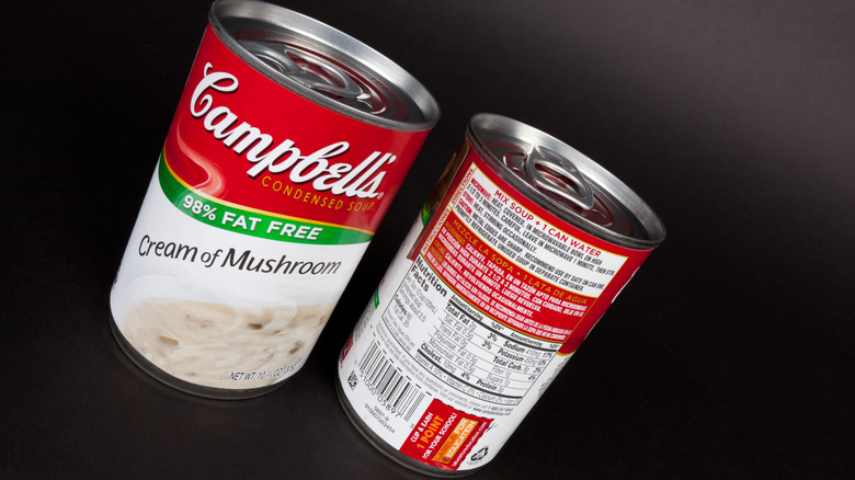 Two cans of cream of mushroom soup rest against a dark background