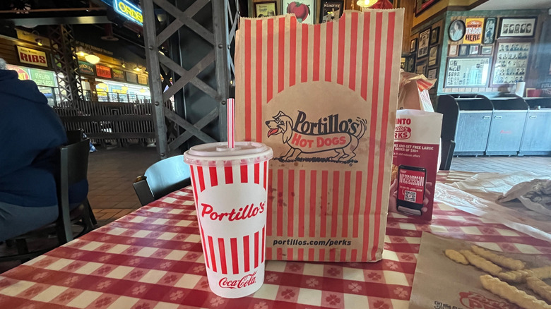 Portillo's cup and paper bag with logos on a table at a restaurant