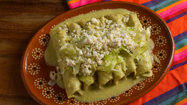A plate of slender green enchiladas, topped with cotija cheese and lettuce.