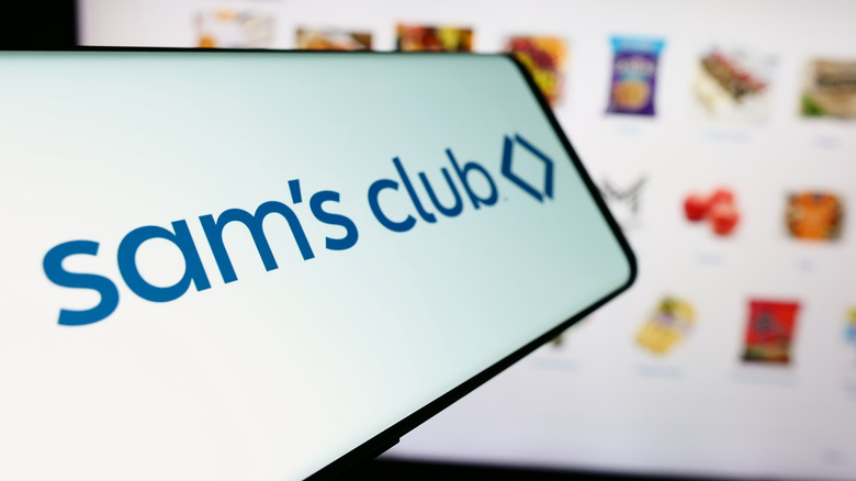 A sideways phone displaying the Sam's Club app is held in front of a computer screen