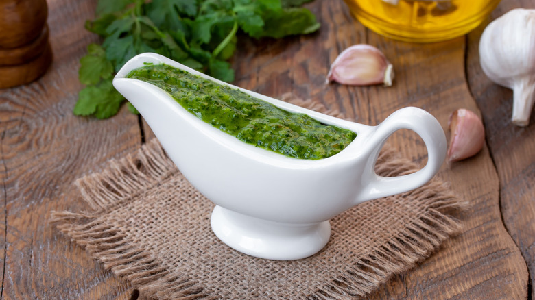 A green sauce in a saucière on a rustic wooden table.