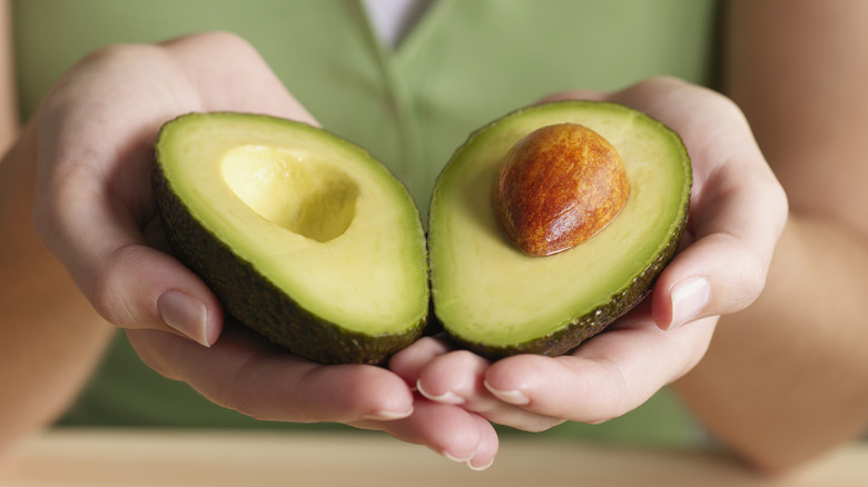 Hands holding green avocado sliced open
