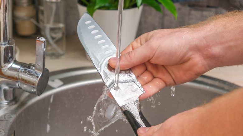 Person washing a knife in a kitchen sink.
