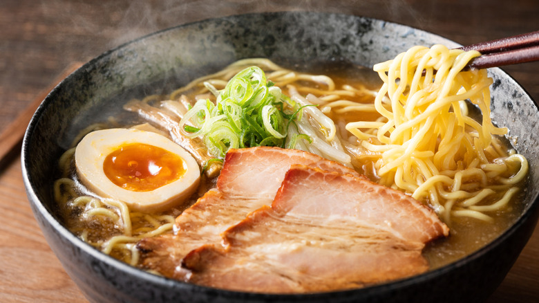 a soy-marinated egg with a jammy yolk sits in a bowl of tonkatsu ramen