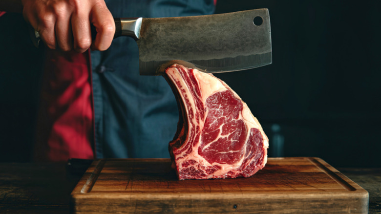 Prime rib on a wooden cutting board being sliced with a meat cleaver.