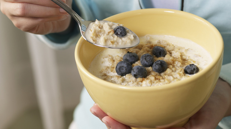 A person eating a bowl of oatmeal with blueberries