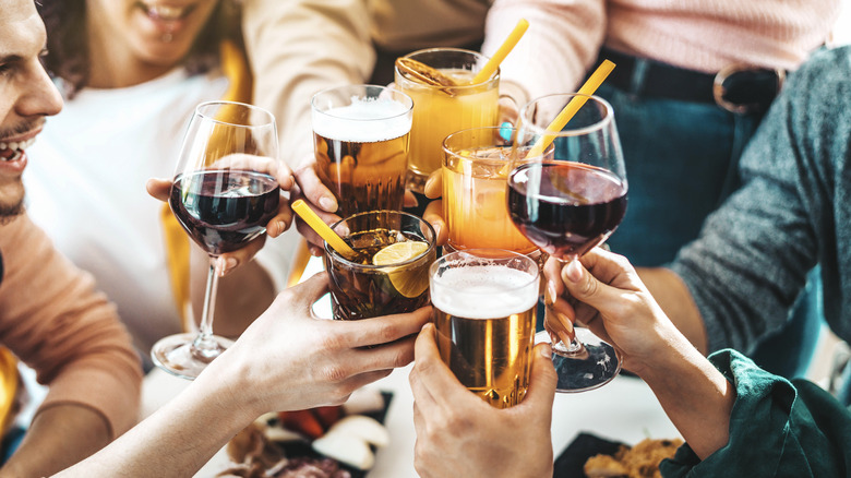 Friends at a gathering each hold a different alcoholic beverage, clanking glasses