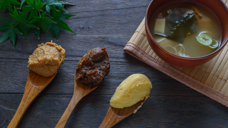 A bowl of miso soup with red, white, and yellow miso pastes on a spoon.