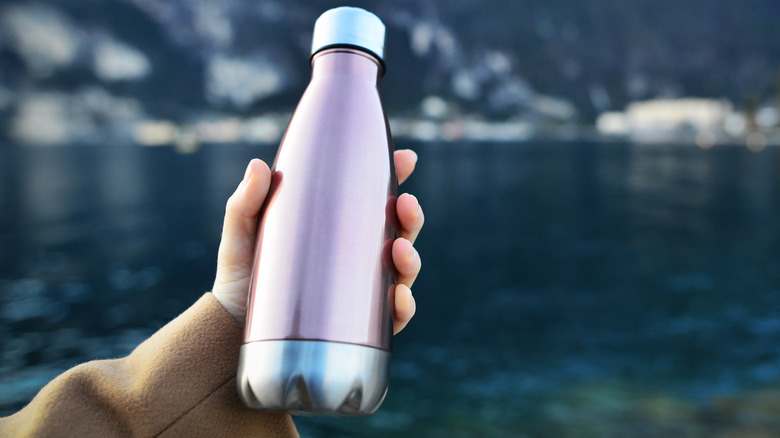 hand holding thermos over lake