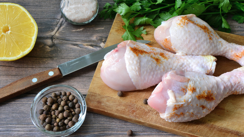 Raw chicken drumsticks on a wooden cutting board.