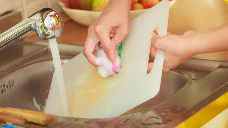 Hands cleaning a plastic cutting board in sink