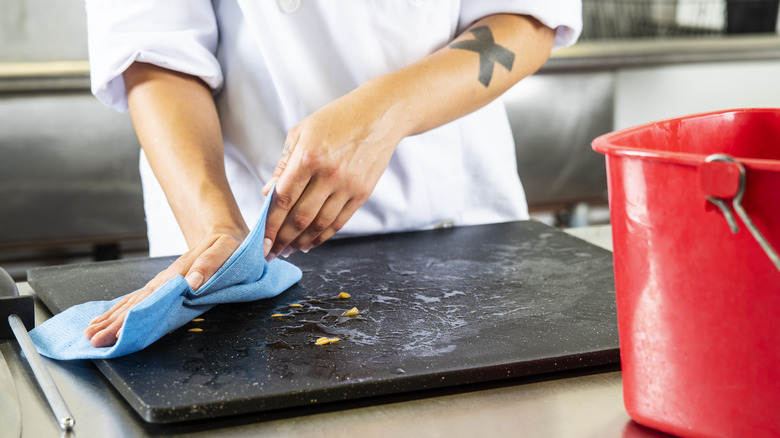 Cleaning a black cutting board with towel and water
