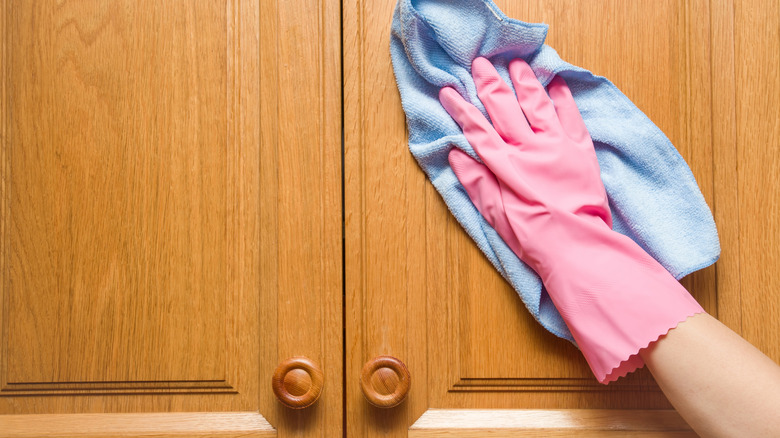 Hand in pink glove wiping a wooden cabinet with a microfiber cloth