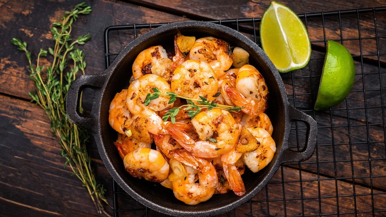 Cooked shrimp in a bowl on a table next to herbs and lime wedges.