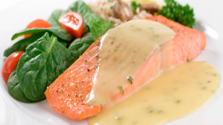 Cooked salmon with a light yellow sauce on a plate next to spinach salad and brown rice with mushrooms.