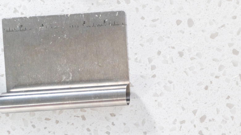 A metal bench scraper sits on a white countertop