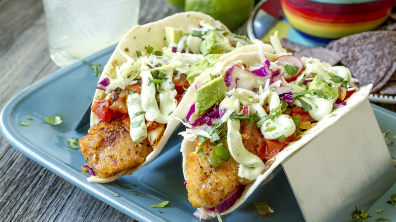 Plate of fish tacos with salsa, avocado, coleslaw, and lime