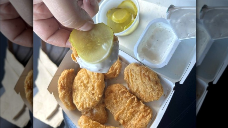 A hand holds a McNugget topped with a pickle slice, dipped in ranch.