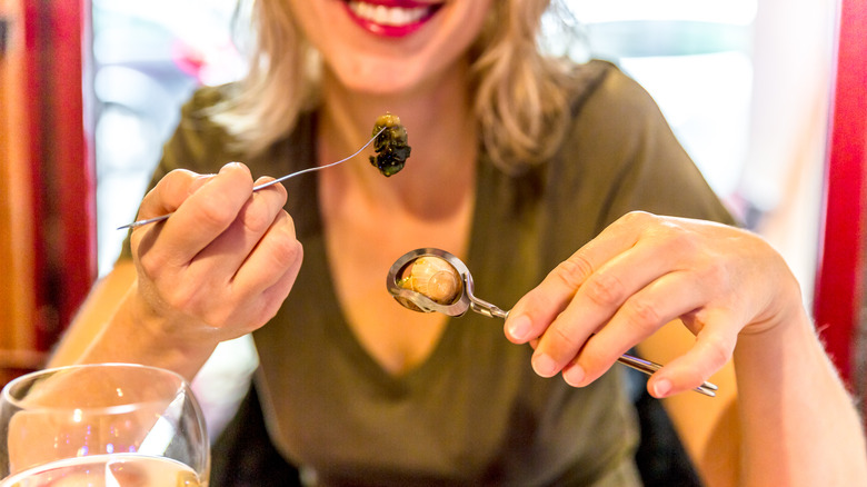 person eating escargot with tongs and fork