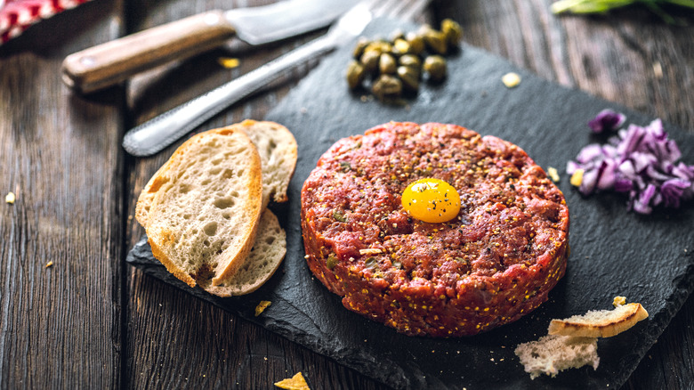 steak tartare on a black slab with toast, capers, diced red onions, topped with a quail egg