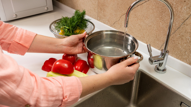 someone holds a pot beneath a running faucet