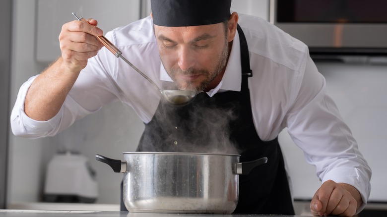A chef tastes a ladle over a steaming pot of soup or stew