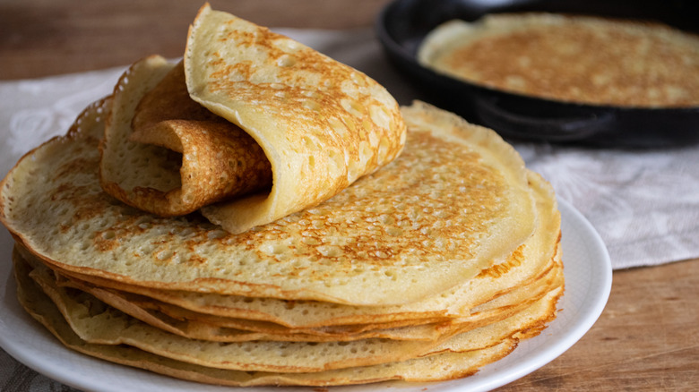 A stack of freshly made crepes sitting on a white plate.