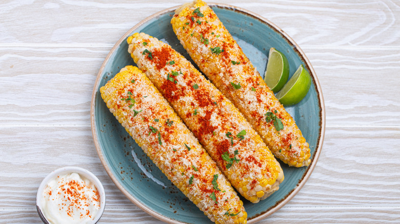 Three corn cobs sprinkled with seasoning and cilantro.
