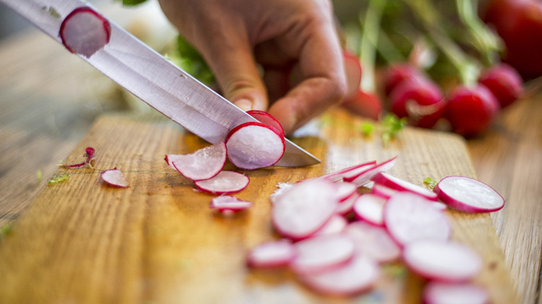 Chopping radishes into slices on a wooden chopping board