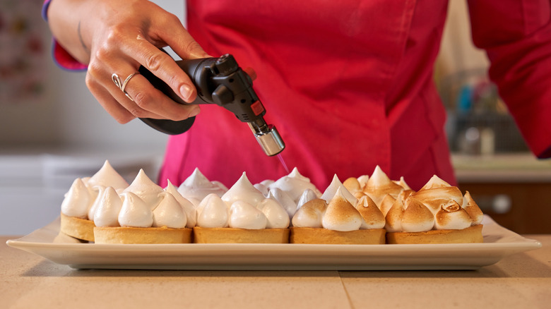 a person using a kitchen torch to toast meringues