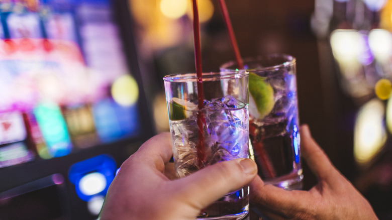 Two people holding drinks at a slots machine.