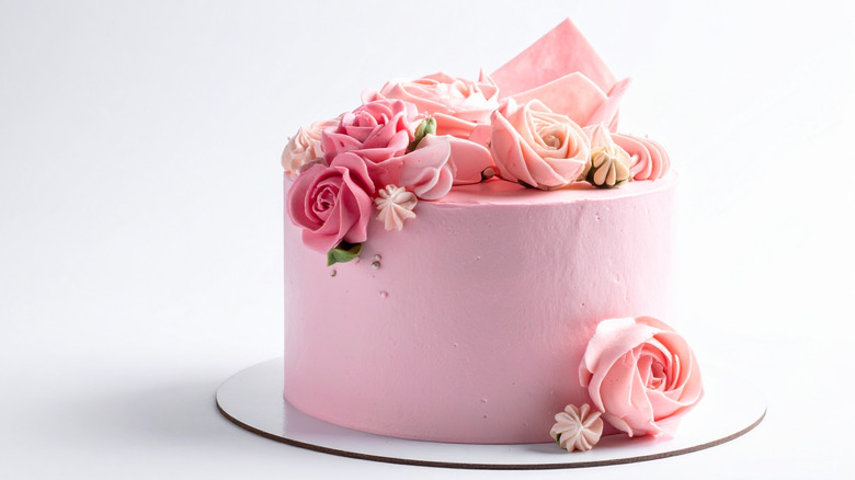 A perfectly frosted pink cake with pink roses made out of frosting.
