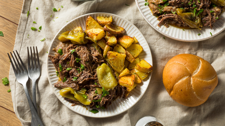 mississippi pot roast on a plate with potatoes and a roll