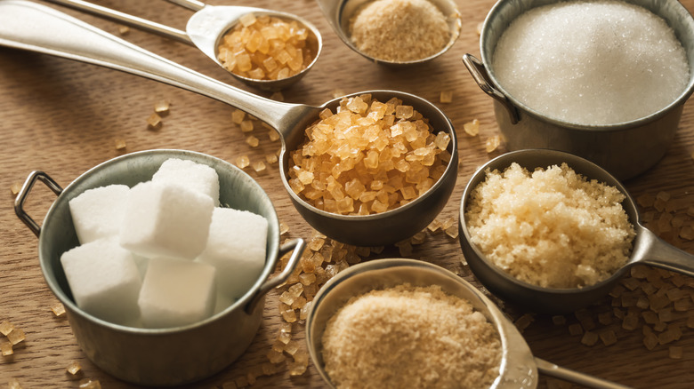 Brown and white granulated sugars in measuring spoons and small metal cups on a wood surface