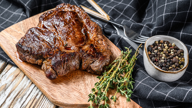 chuck roast on a cutting board next to fresh thyme and a bowl of mixed peppercorns