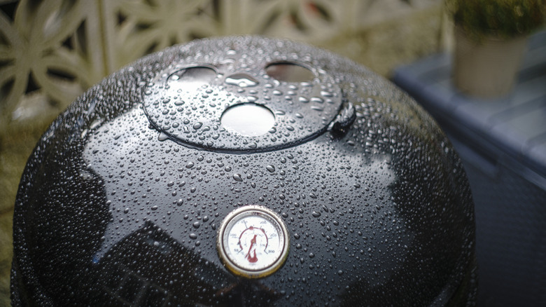Rain collects on the lid of a gleaming black charcoal grill