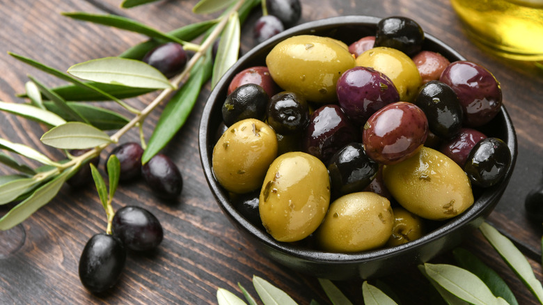 Olives on a branch next to olives in a bowl.
