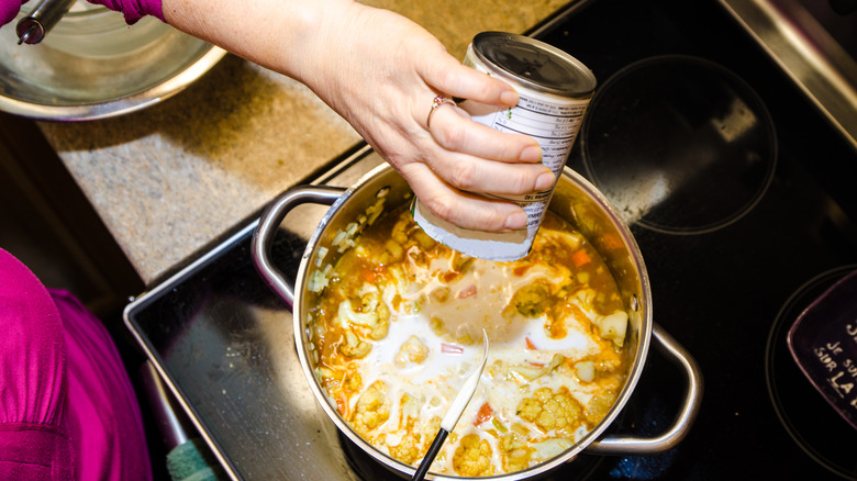 A can of soup being poured into a pot.