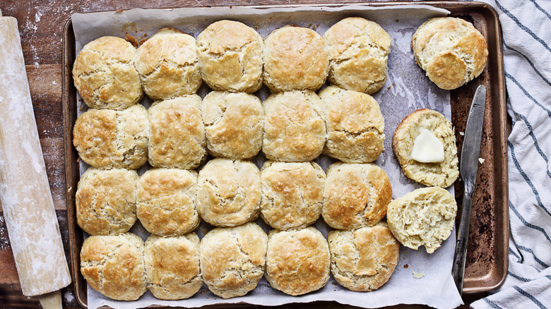 Baked biscuits in a baking pan, with one cut in half with a pat of butter.