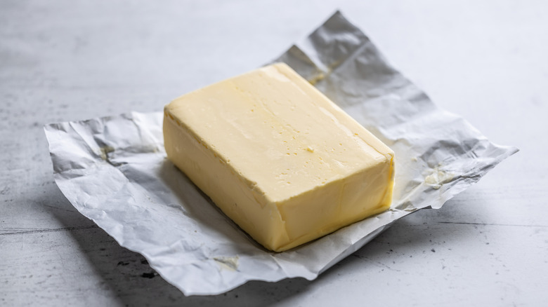 A block of butter sits on its open wrapper on a stone surface