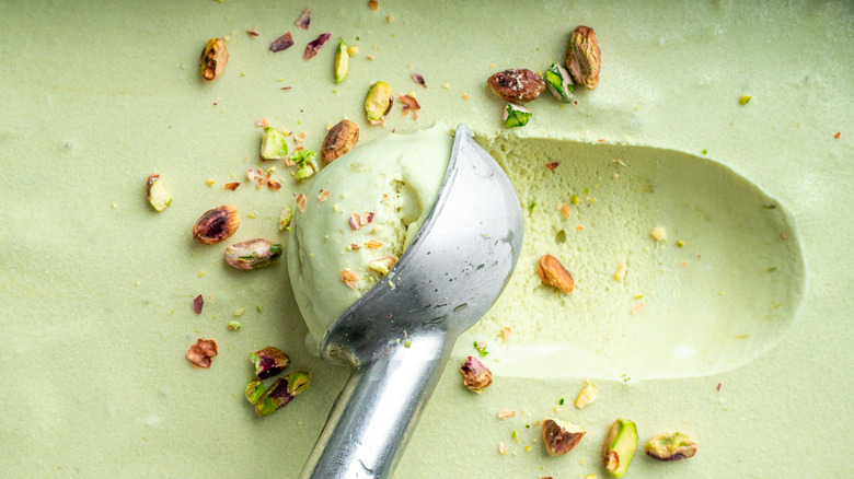 Green ice cream is scattered with chopped and whole pistachios