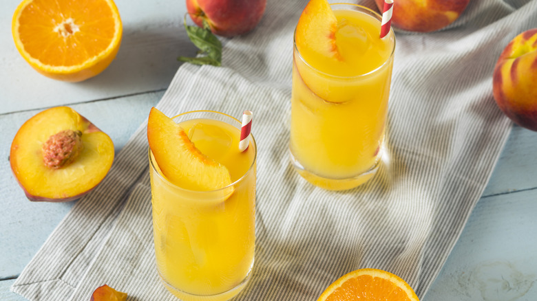 Fuzzy navel drinks next to sliced peaches and a half an orange.